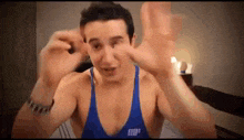 a shirtless man in a blue tank top is making a funny face with his hands .