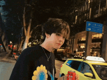 a man in a black shirt with a yellow flower on it holds a can of soda