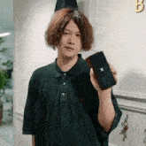 a man in a green polo shirt is holding a cell phone with a x on it