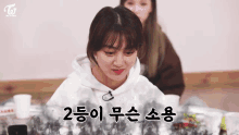 a girl in a white hoodie is sitting at a table with korean writing on it