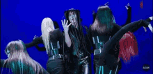 a group of women are dancing in front of a blue background . one of the women is wearing dreadlocks .