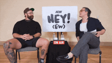 two men are sitting in front of a sign that says hey ( ew )