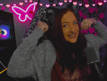 a woman stands in front of a neon butterfly and hearts