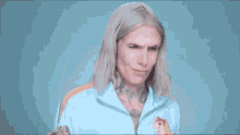 a man with long blonde hair is wearing a light blue jacket with a unicorn on it .