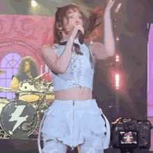 a woman singing into a microphone on a stage with a lightning bolt on the drum set