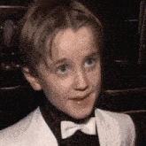 a young boy wearing a tuxedo and bow tie is smiling .