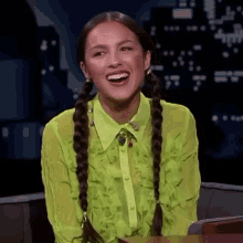 a woman with pigtails is wearing a green shirt and smiling while sitting in a chair .