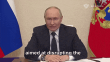 a man in a suit and tie is sitting at a desk with the words " aimed at disrupting the " in front of him