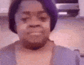 a woman wearing a purple hat and a blue shirt is smiling in a kitchen .