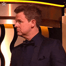 a man in a tuxedo and bow tie is standing in front of a yellow star