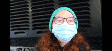 a woman wearing a face mask and glasses is standing in front of a fan