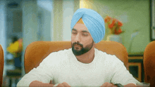 a man wearing a blue turban and a white shirt is sitting at a table .