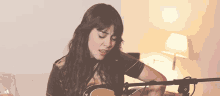 a woman playing a guitar in front of a microphone