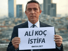 a man in a suit and tie holds a sign that says ali koc istifa