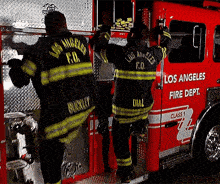 two firefighters from the los angeles fire department climb into a red fire truck