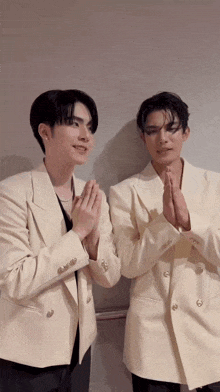 two men in white suits are standing next to each other with their hands folded .