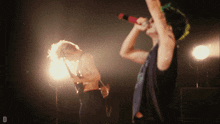a man singing into a microphone while another man plays a guitar in the background