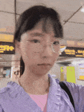 a girl wearing glasses and a purple shirt stands in front of a sign that says ' subway ' on it