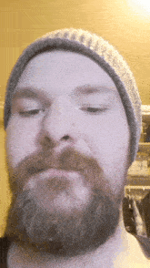 a man with a beard is wearing a beanie and making a funny face