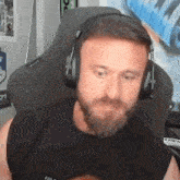 a man with a beard is wearing headphones while sitting in a gaming chair .