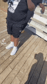a man is standing on a wooden deck wearing a black shirt and white shoes .