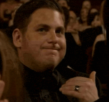 a man in a tuxedo is giving a thumbs up in front of a crowd .