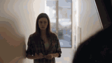 a woman in a plaid shirt stands in a hallway