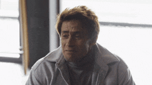 a man wearing a turtleneck and a white jacket is looking down