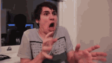 a man in a gray shirt is making a funny face with his mouth open .