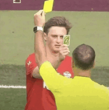 a man in a red shirt is getting a yellow card from a referee while holding a uno card .