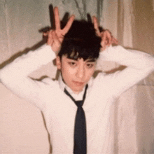 a young man wearing a white shirt and black tie is making a peace sign