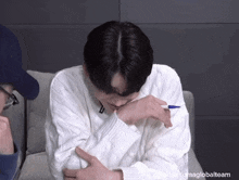 a young man in a white sweater is sitting on a couch with a pen in his hand .