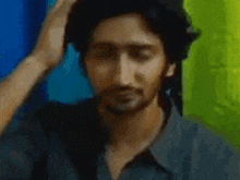 a man with a beard is scratching his head with his hand in front of a green curtain .