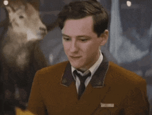 a man in a brown suit and tie stands in front of a stuffed animal