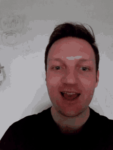 a man 's face is against a white wall with drawings on it including one that says whistle
