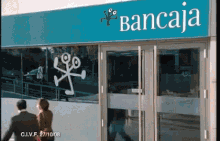 a man and woman walk in front of a bancaja store