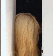 a woman with long blonde hair is standing in a doorway and looking out .