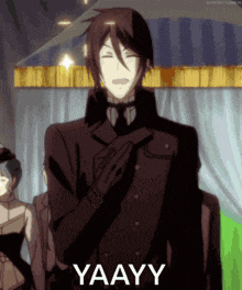 a man in a black suit says yaayy while smiling