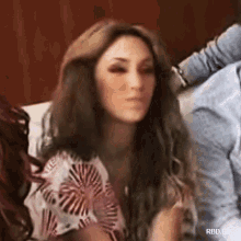 a woman with long brown hair is sitting on a couch and making a funny face .