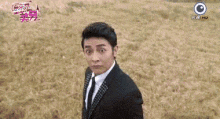 a man in a suit and tie is standing in a field and making a face .