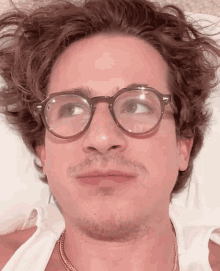 a man wearing glasses and a necklace looks at the camera