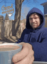 a man in a blue hoodie is holding a cup of coffee with the words good morning written in the background