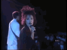 a woman with red hair is singing into a microphone while a man in a white shirt stands behind her ..
