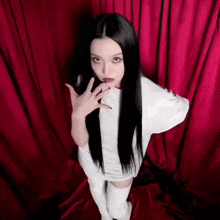 a woman with long black hair wearing a white shirt and white knee high socks stands in front of a red curtain