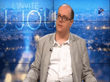 a man in a suit is sitting in front of a screen that says l' invite jour