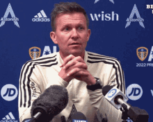 a man stands in front of microphones in front of a blue background that says wish