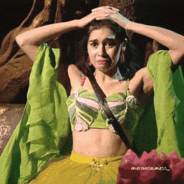 a woman in a green top and yellow skirt holds her head in her hands