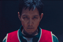 a close up of a man 's face with a red and green vest