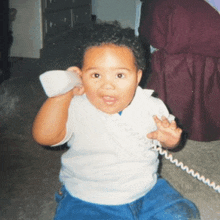 a young child is sitting on the floor talking on a phone