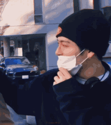 a man wearing a mask and a beanie is standing in front of a blue mustang